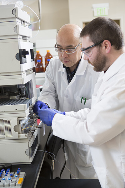 Dr. Lee (left) and Lab Assistant Zack Cizek prepare equipment for a pharmaceutical product manufacturing lab.